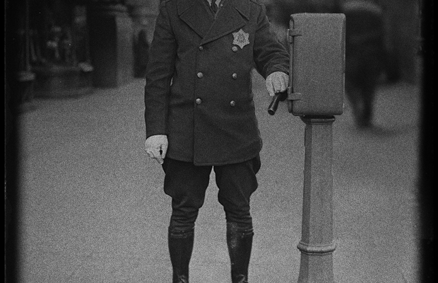 A dimanian LPD officer in a early LPD uniform stands next to a new call box.