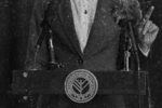 Closeup of the mayor standing at a podium, the Lovat City Seal is visible on the front.