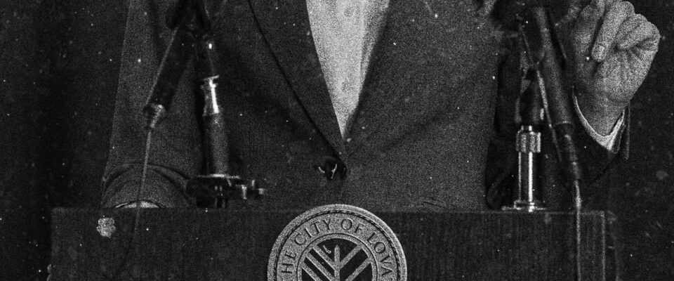 Closeup of the mayor standing at a podium, the Lovat City Seal is visible on the front.